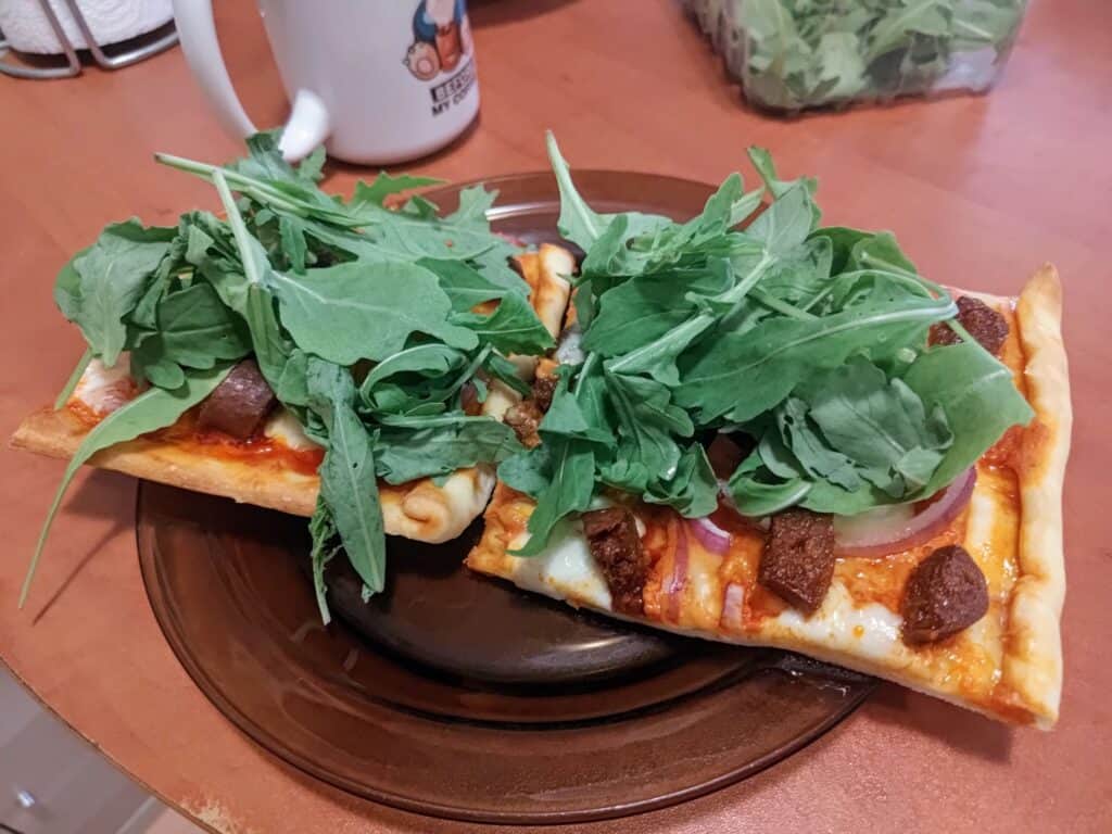 Zdjęcie pizzy z czerwonym pesto, mozarellą, chorizo i niewielkim dodatkiem miodu pokrytej rukolą