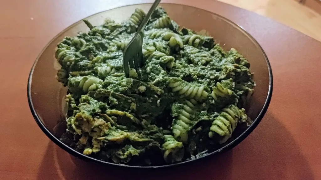 Makaron fusilli z gęstym, zielonym sosem warzywnym i pieczonym tofu w szklanym talerzu.
