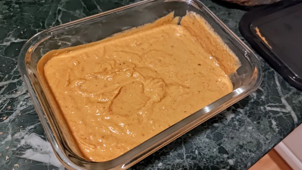 Gładka, pomarańczowa pasta z awokado, serka wiejskiego i papryki w szklanym pojemniku.