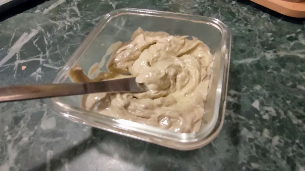 Gęsta pasta z awokado, serka wiejskiego i czosnku w szklanym pojemniku, z nożem.