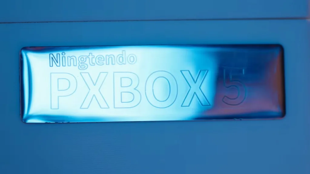 Napis "Ningtendo PXBOX 5" wygrawerowany na błyszczącej, metalicznej powierzchni w kolorze niebieskim.