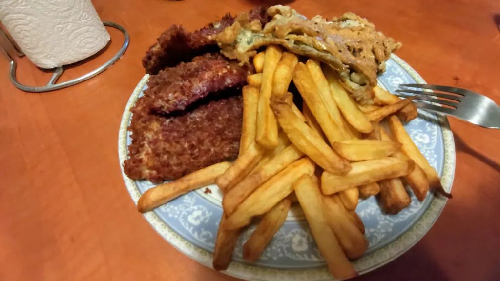Smażony dorsz w fioletowej panierce panko podany z dużą ilością frytek na talerzu.