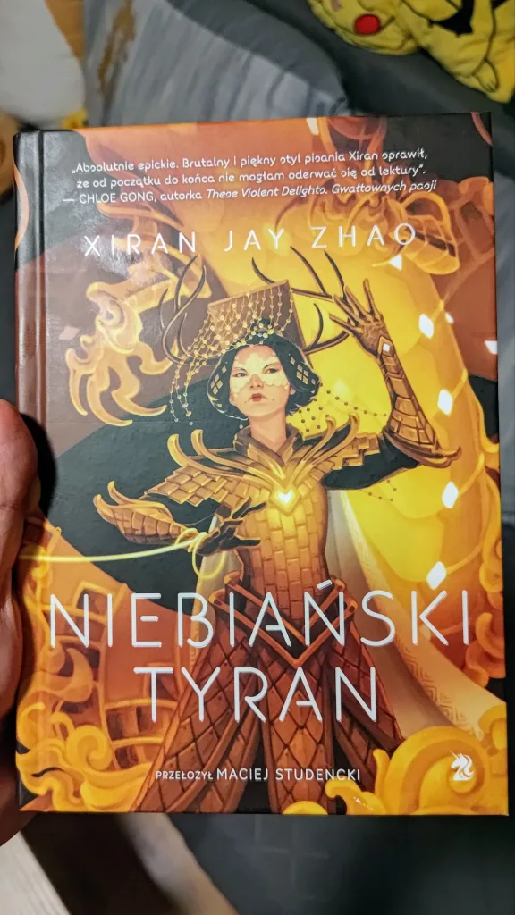 Okładka książki pod tytułem „Niebiański Tyran” autorstwa Xiran Jay Zhao trzymana w dłoni.