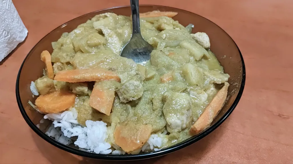 Talerz z domowym zielonym curry z ryżem i kawałkami marchwi oraz widelcem wbitym w potrawę.