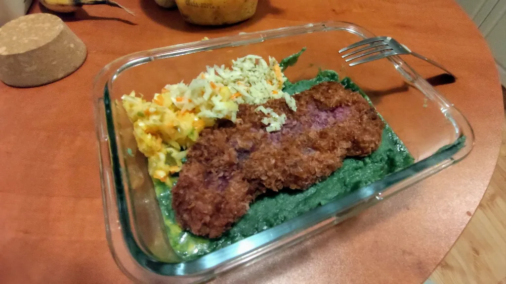 Kotlet panierowany z purpurowym wnętrzem, podany na zielonym puree z dodatkiem surówki.