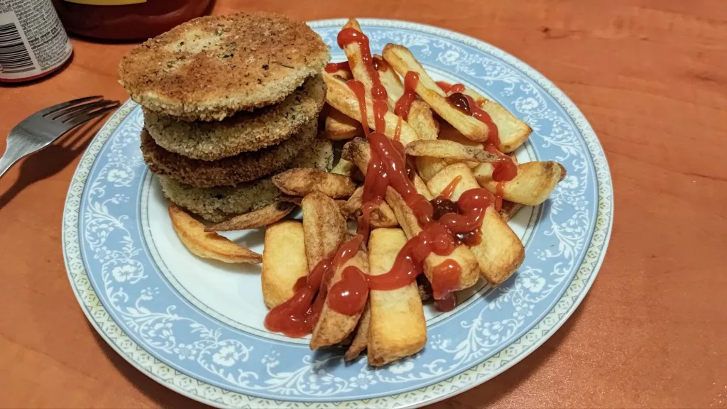 Stos panierowanych kotletów podany z frytkami i keczupem na talerzu.