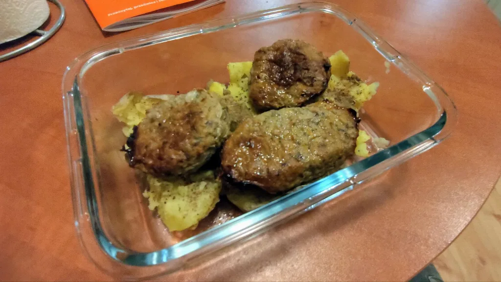 Trzy kotlety mielone podane z ziemniakami w szklanym pojemniku na brązowym blacie.