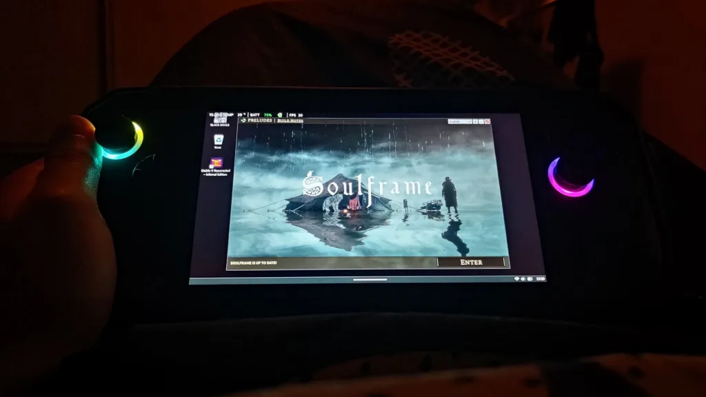 Gracz trzymający urządzenie do gier z podświetlanym joystickiem, na ekranie widoczny jest tytuł gry Soulframe