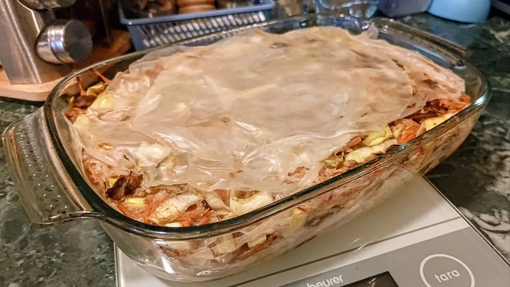 Naczynie żaroodporne z zapiekanką przykrytą papierem do pieczenia, stojące na wadze kuchennej.