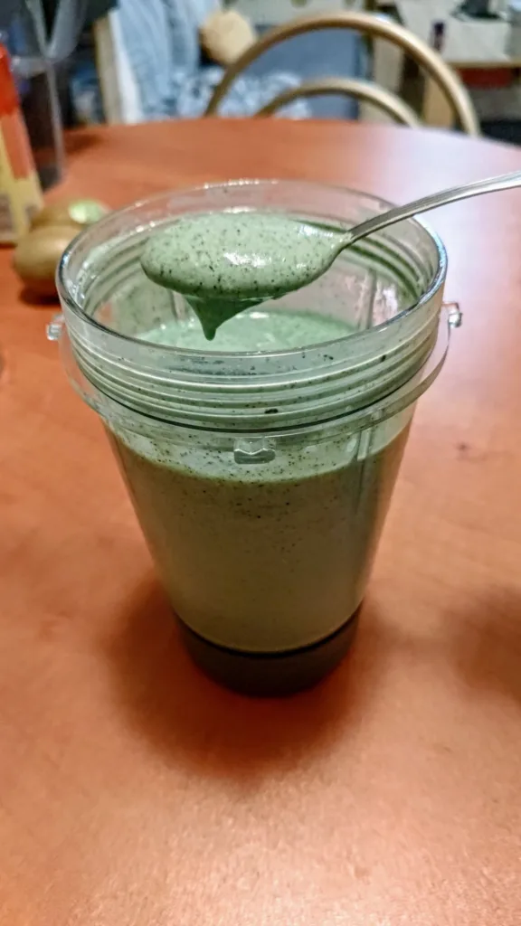 Łyżka z zielonym smoothie nad kielichem blendera