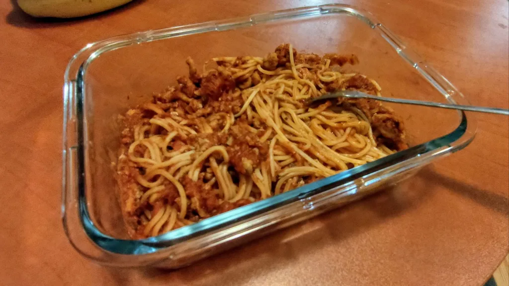 Szklane naczynie z makaronem spaghetti i sosem bolońskim, widoczne są nitki makaronu i kawałki mięsa w sosie.
