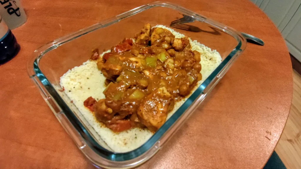 Danie z kurczakiem w sosie curry podane na kaszy kuskus w szklanym pojemniku.