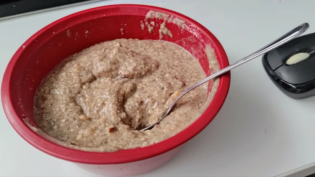 Miseczka z czerwonego plastiku wypełniona owsianką lub puddingiem z nasion chia, z widocznym metalowym widelcem.