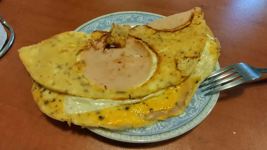 Omlet z plastrami szynki i serem na talerzu, obok widelca.