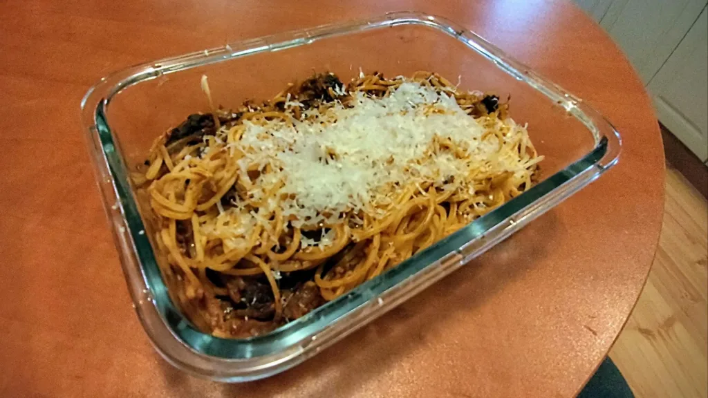 Porcja spaghetti z suszonymi śliwkami i startym serem w szklanym naczyniu