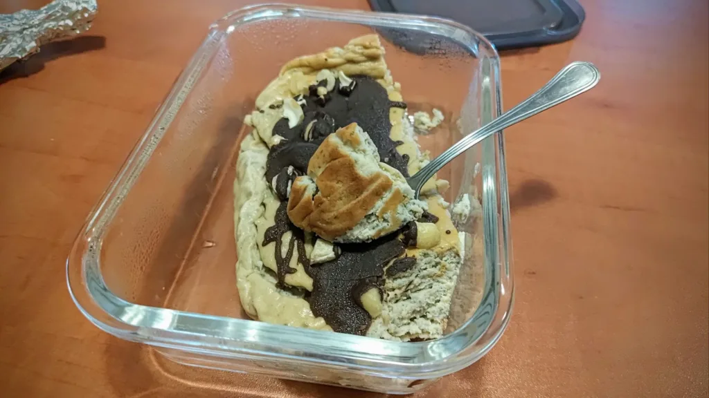 Ciasto z polewą czekoladową i kawałkami ciasta w szklanym naczyniu, z widelcem w środku.