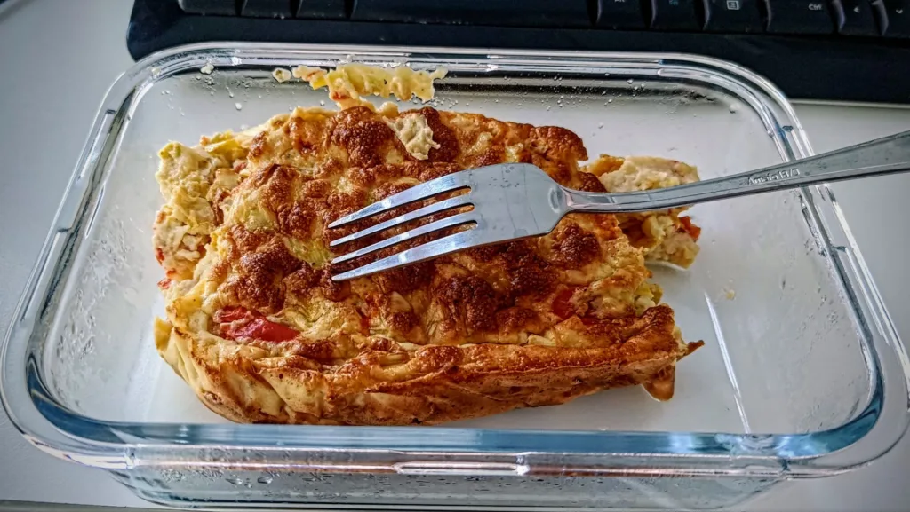 Złocisty omlet z papryką i potem w szklanym naczyniu, z widelcem wbitym w środek.