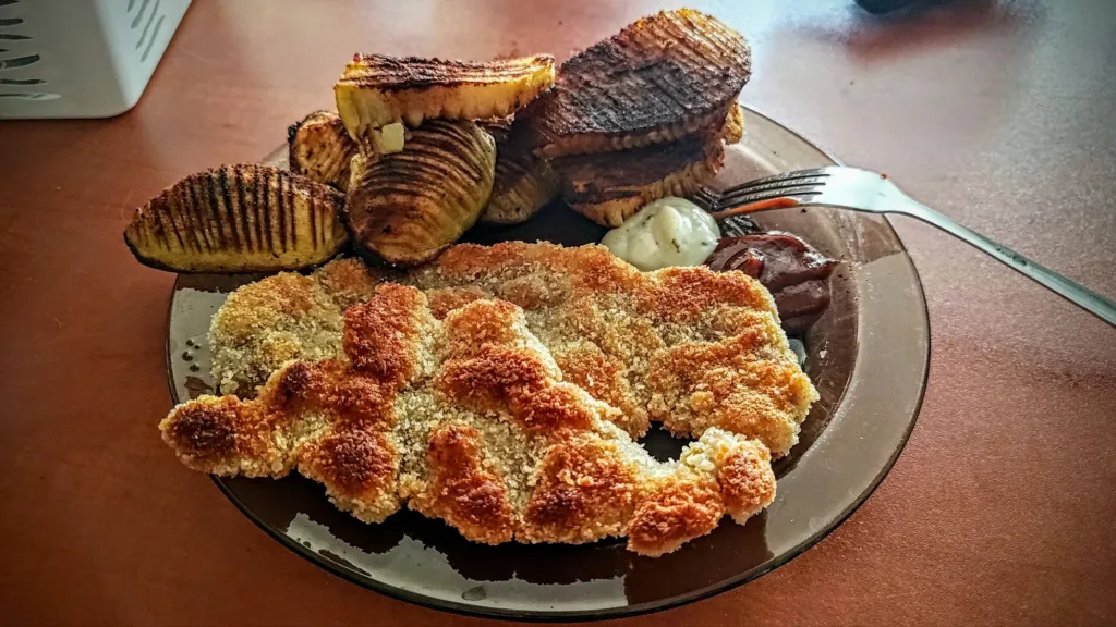 Talerz z panierowanym kotletem, ziemniakami hasselback i sosami.