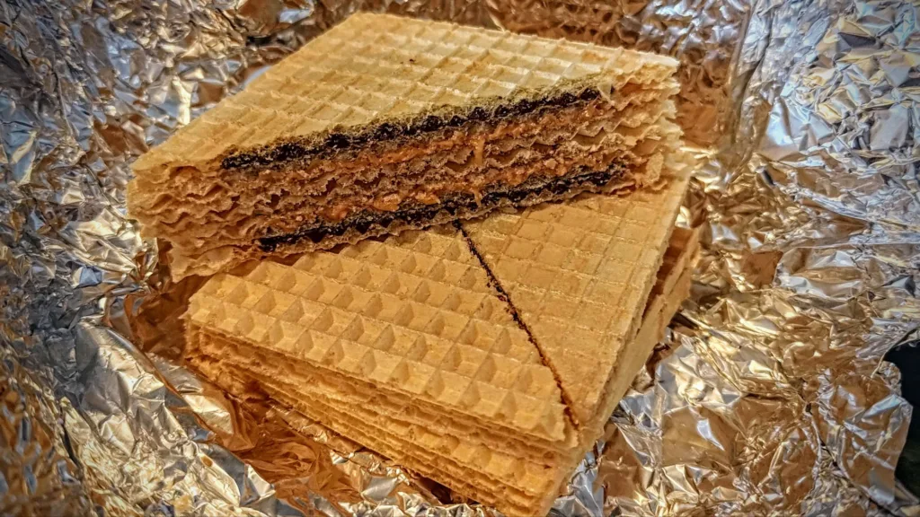 Zbliżenie na stos wafli z kremem czekoladowym i orzechowym, owiniętych w pogniecioną folię aluminiową.