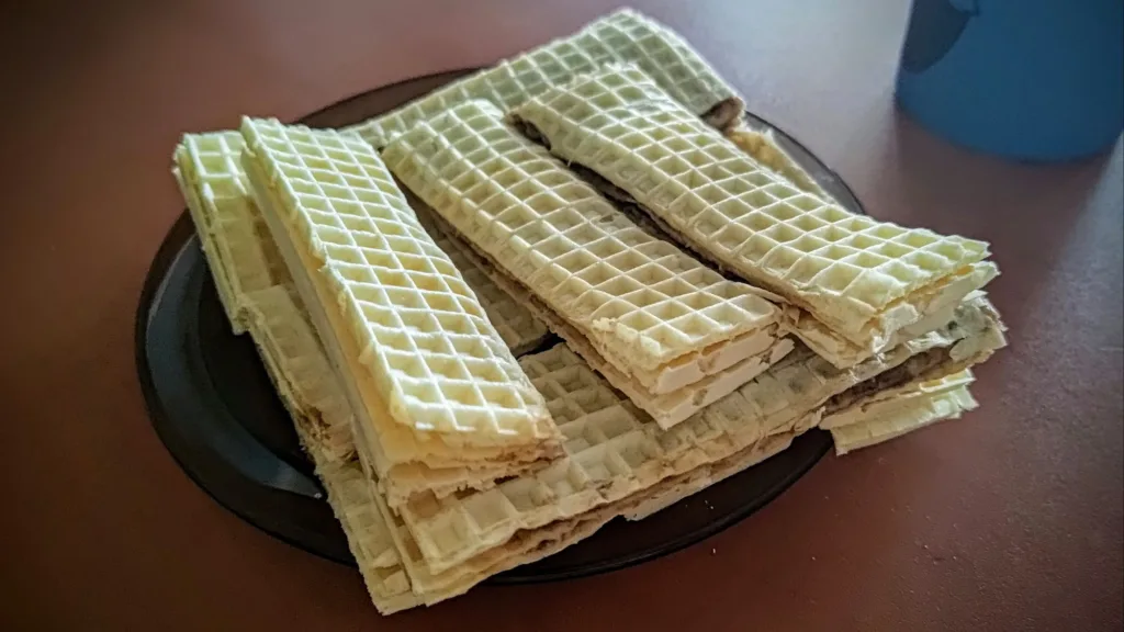 Stos wafli przekładanych kremem na ciemnym talerzu.