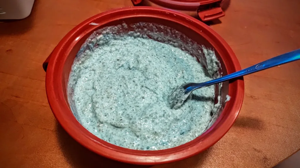 Niebieski deser z nasionami chia w czerwonej misce, z niebieską łyżką.