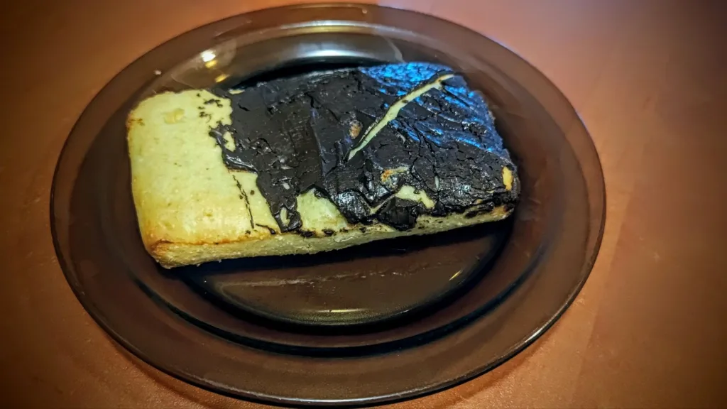 Kawałek ciastka z polewą czekoladową na ciemnym talerzu.