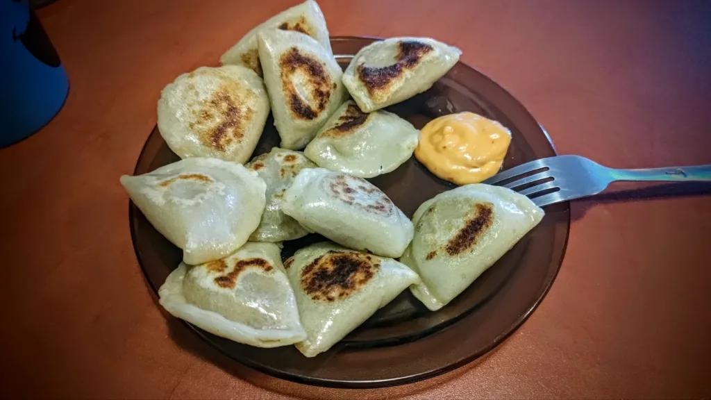 Talerz z pierogami, niektóre lekko przypieczone, z dodatkiem sosu i widelcem.