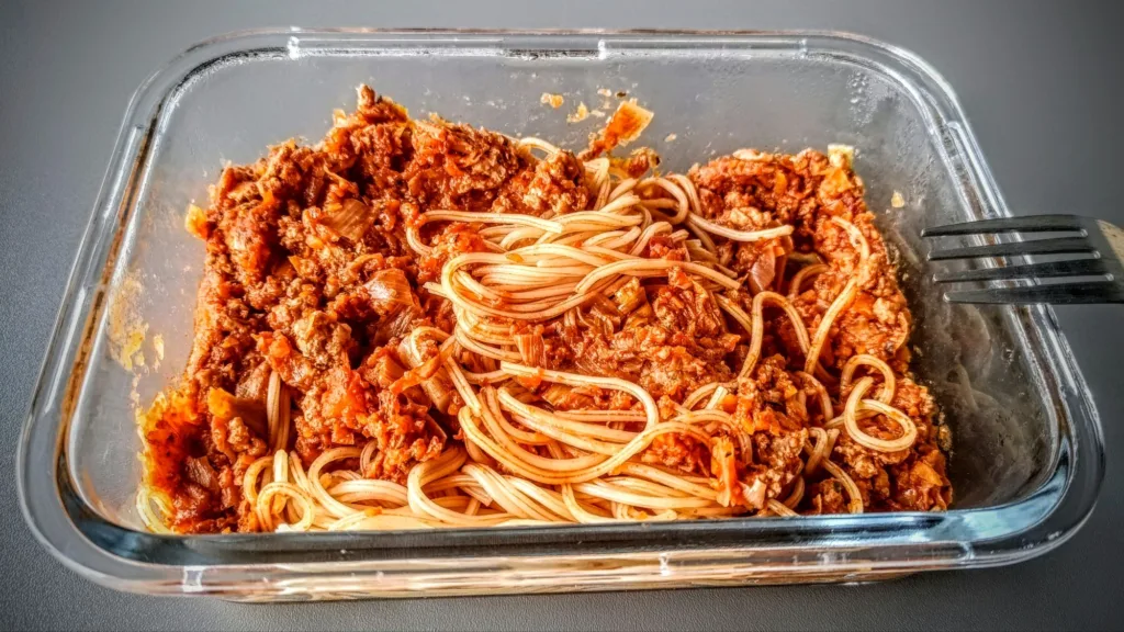 Porcja spaghetti bolognese w szklanym pojemniku z widelcem