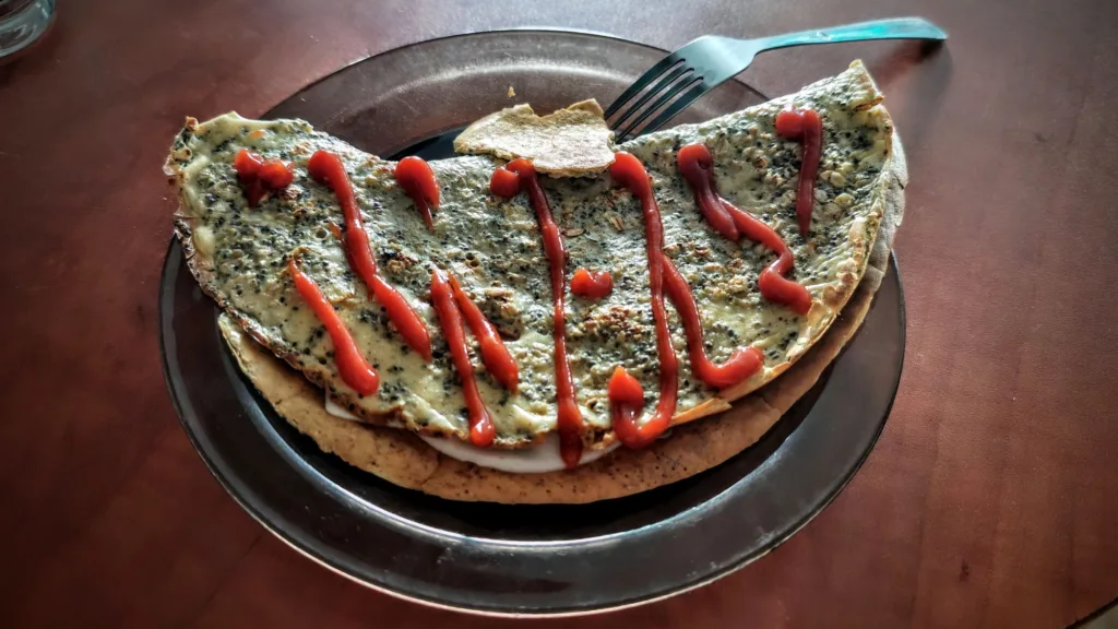 Omlet z serem i ketchupem na talerzu, obok widelca