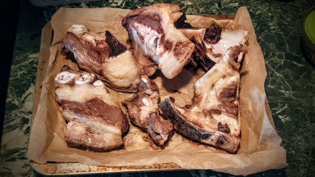 Kilka porcji surowego mięsa z widocznymi kośćmi, ułożone na papierze do pieczenia na blaszce.