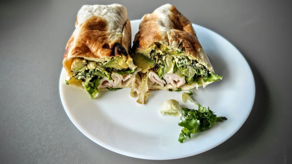 Przekrojony wrap z indykiem, sałatą i awokado na białym talerzu