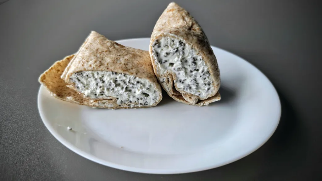 Wrapy pokrojone na pół, wypełnione kremowym farszem z nasionami chia, podane na białym talerzu.