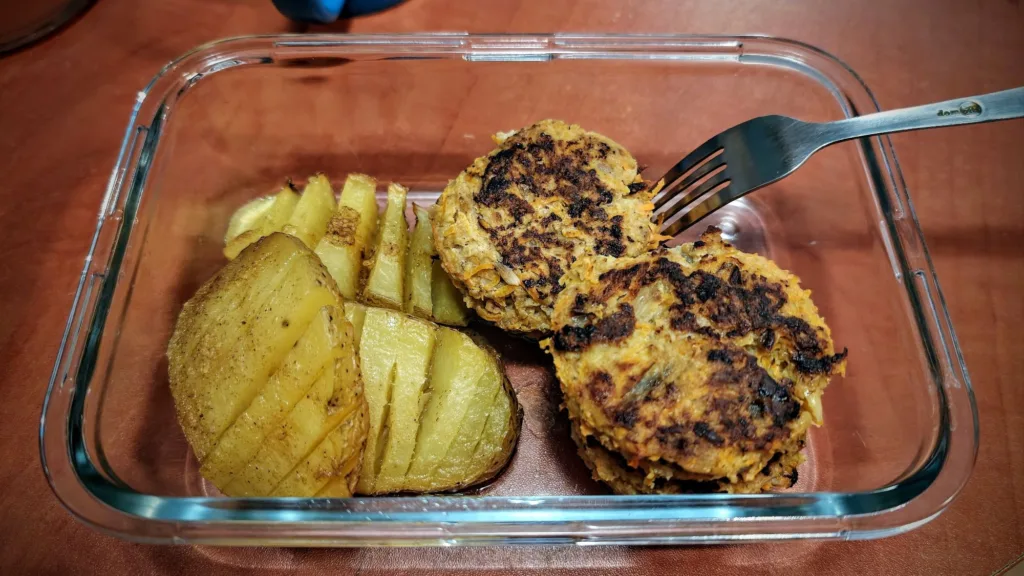 Dwa kotlety i pieczone ziemniaki w szklanym naczyniu, obok leży widelec.