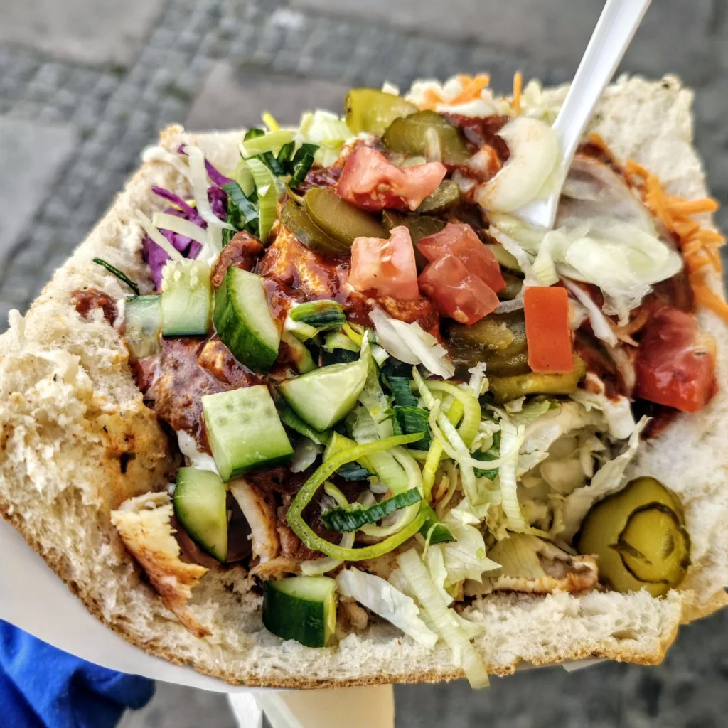 Duży kebab w chlebie pita z mięsem, pomidorami, ogórkami, czerwoną i białą kapustą oraz sosem.